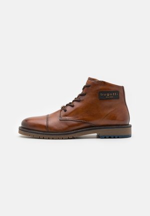 Bruine lederen enkelboot met ronde teen, vetersluiting en merkdetail. Gelaagd oppervlak en contrasterende bruine zool met blauwe accenten.