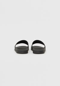 Valgte sorte flade sandaler med to buede stropper. Tekstureret sål og glat ydersål. Simpelt design, let vægt, og minimalistisk udseende.