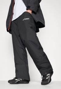 Pantalones impermeables negros de corte holgado, con una cintura elástica, bolsillos laterales y un prominente logo blanco de TERREX en el muslo izquierdo.