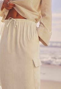 Falda de color crema, ligera, con cintura fruncida, cordón y bolsillo lateral. Presenta una textura suave y un ajuste relajado.