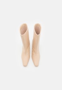 Beige nahkasaappaat, jotka ylettyvät polven korkeudelle, terävän kärjen ja sileän, mattaisen pinnan kanssa. Saumaton muotoilu, jossa on leveä, suora aukko ylhäällä.