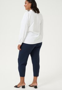 Valkoinen pitkähihainen paita puffiolkain kanssa ja takasauma, yhdistettynä laivastonsinisiin slim-fit-housuihin. Mustat korkokengät viimeistelevät asun.