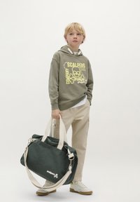 Szary sweatshirt z żółtą grafiką, beżowe spodnie cargo i zielona torba canvas z białymi paskami. Casuowe obuwie z białą bazą.