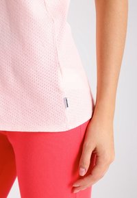 Camicia corta rosa chiaro a maniche corte realizzata in tessuto a rete traspirante, con un piccolo etichetta con logo all'orlo, abbinata a leggings rosa.