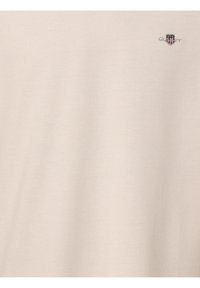 Beige tekstureret t-shirt med et lille broderet logo øverst til venstre. Fremstillet af blødt, behageligt stof med et afslappet design.