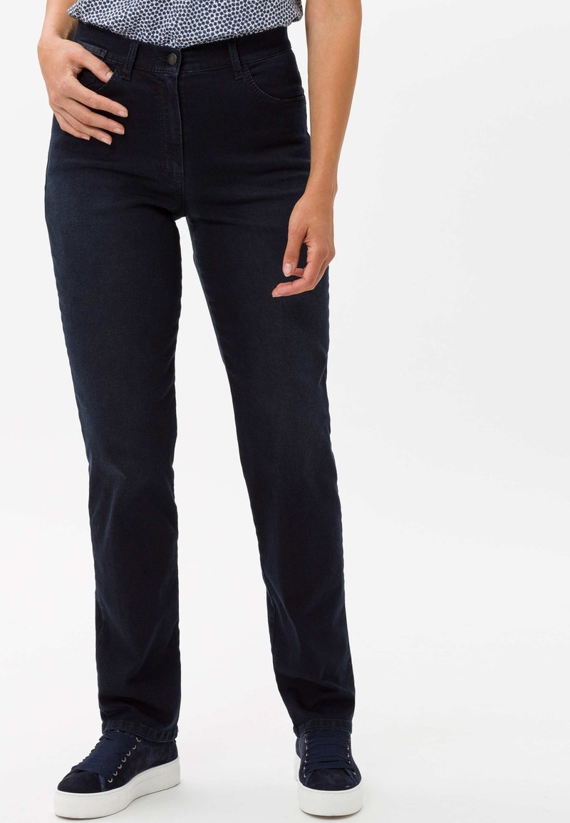 Donkerblauwe spijkerbroek van denim, met een strak ontwerp, standaard zakken en een klassieke knoopsluiting. Gecombineerd met donkere sneakers.