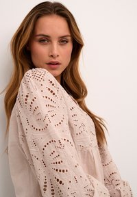 Pale pink blouse with intricate embroidery and cut-out details. Soft, flowing fabric with puffed sleeves and a relaxed fit design.