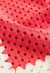 Coperta all'uncinetto in corallo e bianco, con un motivo geometrico a trama aperta e bordi ondulati. Tessuto morbido e lavorato a maglia.