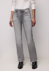 Grijze flare jeans met een taille op middelhoog niveau, voorzakken en subtiele vervaging. Gecombineerd met zwarte enkellaarzen voor contrast.