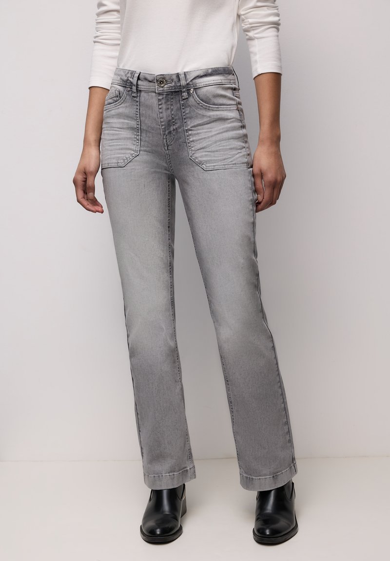 Grijze flare jeans met een taille op middelhoog niveau, voorzakken en subtiele vervaging. Gecombineerd met zwarte enkellaarzen voor contrast.