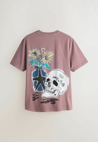 T-shirt en coton mauve avec un motif graphique représentant un crâne et un vase de fleurs. Le vase est bleu avec un motif d'étoiles, et les fleurs sont jaunes.