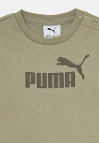 Olivgrön PUMA t-shirt med ribbade ärmslut, med en stor svart logotryck och två tryckknappar på axeln för enkel påtagning.