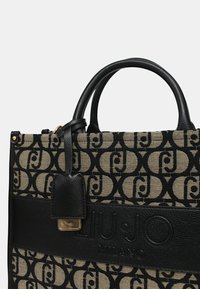 Borsa a tracolla nera e beige con un motivo testurizzato, dettagli in pelle, doppi manici superiori e un logo prominente su una fascia liscia.