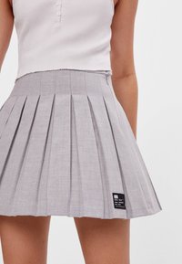 Šedá plisovaná sukně z texturované látky s visačkou. Má vypasovaný pás a rozšířený střih, sahající do poloviny stehen.