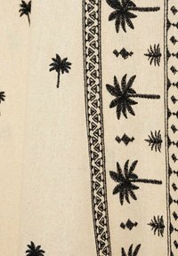 Tissu brodé avec un fond crème orné de motifs de palmiers noirs et de motifs géométriques le long des bordures, mettant en valeur la texture et les détails.