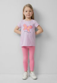 Lila Baumwoll-T-Shirt mit einem Pailletten-Schmetterlingsdesign in Orange und Pink, kombiniert mit rosa Leggings und weißen Sneakern.
