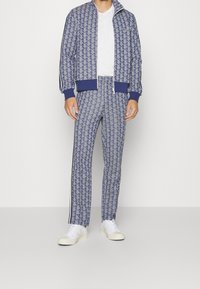 Mörkblå och ljusblå mönstrad träningsoverall med en jacka med dragkedja och matchande byxor, tillverkad av ett mjukt tyg, kombinerad med vita sneakers.