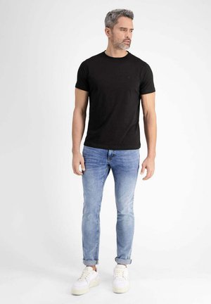 Schwarzes enges T-Shirt, blaue Slim-Fit Jeans und weiße Sneakers. Glatter Stoff, lässiges Design, aufgerollte Säume an den Jeans, schlichte Stil.