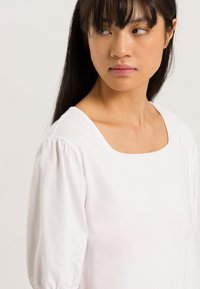 Top bianco a maniche corte con scollatura quadrata e maniche a sbuffo. Il tessuto appare morbido e leggero, con una texture liscia.