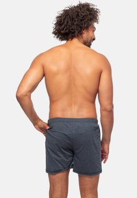 Heren grijze katoenen shorts met een elastische tailleband, een zachte textuur en een zichtbare achterzak. Model zichtbaar vanaf de achterkant.