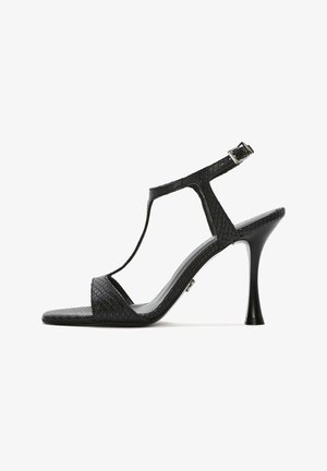 Black high-heeled sandal with a textured reptile pattern, T-strap design, silver hardware buckle, and sleek pointed toe.