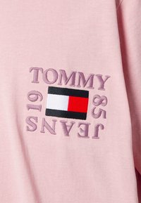 Różowa bawełniana bluza z kapturem z haftem "TOMMY JEANS" w lawendowym kolorze oraz naszywką z logo w kolorach czerwonym, białym i czarnym.