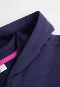 Kołnierzyk polo w kolorze granatowym o gładkiej fakturze, z różową metką po wewnętrznej stronie, starannie przeszyty i ukształtowany.