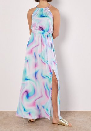 Femme en robe maxi sans manches à motifs tourbillonnants pastel, fente latérale et fines bretelles, portant des sandales plates dorées.