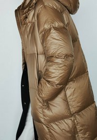 Cappotto lungo in tessuto metallico lucido marrone con cappuccio, caratterizzato da sezioni trapuntate, tasche laterali e chiusura centrale con zip.