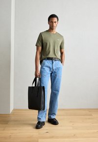 Sort læder tote taske med flade håndtag, båret med en olivengrøn t-shirt og lyseblå jeans, suppleret med sorte sko.