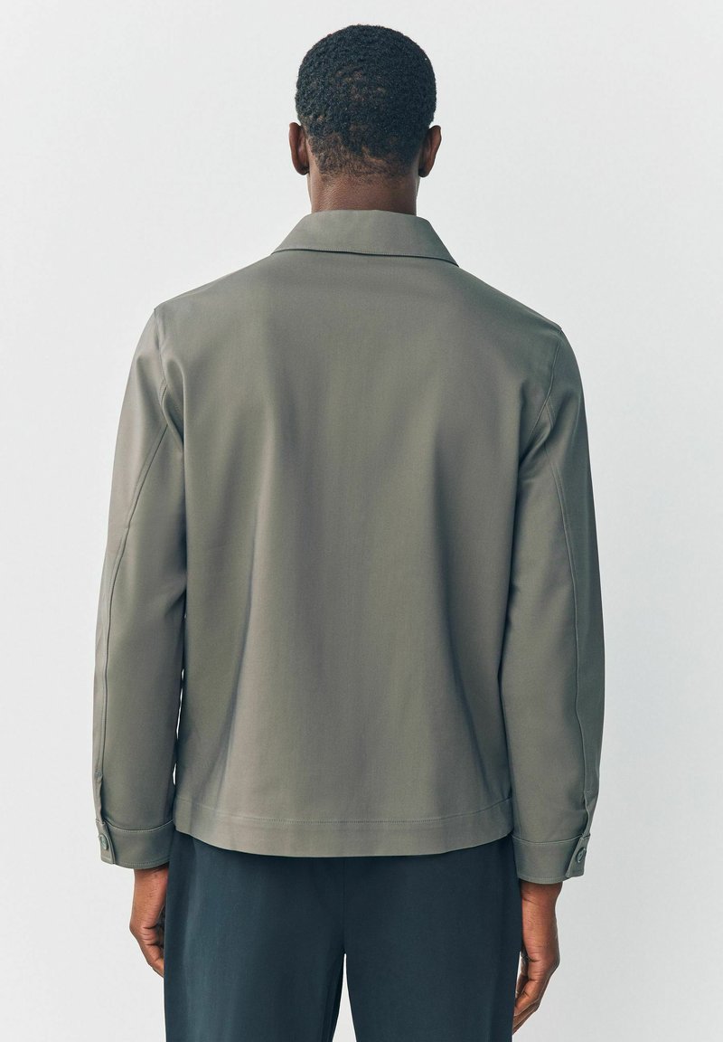 Olivengrüne Jacke mit glatter Textur, lockerer Passform und Reverskragen. Mit langen Ärmeln und geknöpften Manschetten.