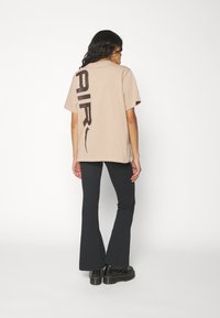 Beige, nagyméretű póló, hátul nagy fekete "AIR" felirattal, fekete harangnadrággal és tömzsi fekete platformcipővel párosítva.