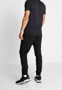 Svart tränings t-shirt med korta ärmar, ihop med svarta joggers. Man som bär sportiga svarta skor med vita accenter.