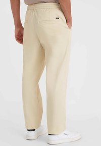 Pantalons beiges à enfiler avec taille élastique, jambes droites, poches arrière et subtile couture décorative. Associés à des baskets blanches.