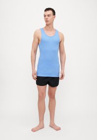 Light blue cotton tank top with wide straps, paired with black shorts, standing on bare feet. Simple, close-fitting design.