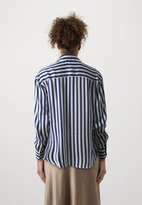 Collared shirt featuring blue and white vertical stripes, long sleeves, and a curved hem, made from smooth, lightweight fabric.