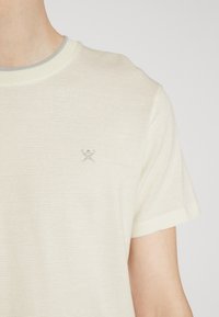 Lys creme farvet kortærmet t-shirt med en tekstureret overflade, ribbet halsudskæring og en lille broderet detalje på brystet.