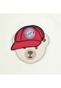 Embroidered bear design in cream fabric, wearing a red cap featuring "FC Bayern München" logo and blue diamond pattern, with textured fur details.