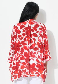 Kimono floral en blanc avec un motif de fleurs rouges vives, en tissu léger, coupe ample, manches mi-longues et fentes latérales.