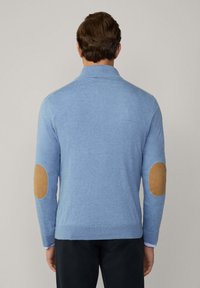 Niebieski sweter z dzianiny z wysokim kołnierzem i długimi rękawami. Posiada jasnobrązowe naszycia na łokciach, ściśle wykończone rękawy oraz dół. Miękka struktura.