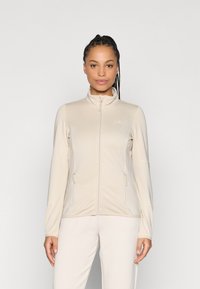 Veste beige à manches longues avec un col montant, une fermeture éclair à l'avant et des poches latérales. Texture lisse avec des détails de panneaux contrastants.