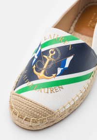 Espadrille en toile avec semelle en jute tissé, arborant des rayures vertes et bleu marine, une ancre dorée avec corde, des drapeaux nautiques et le texte "Ralph Lauren".