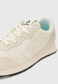 Sneakers bej cu un superior din suede și material sintetic, având un logo alb în formă de stea, închidere cu șireturi și o talpă texturată din cauciuc negru.