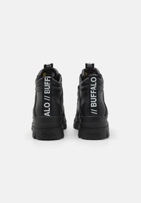Black high-top sneakers with textured leather, featuring a thick rubber sole and a prominent white logo strap on the heel. Vegan material.