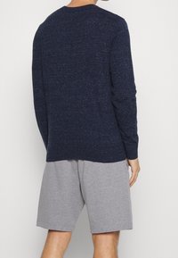 Námořnický pletený svetřík s dlouhým rukávem a strukturovaným povrchem, spárovaný se šedými bavlněnými šortkami. Svetřík má kulatý výstřih a volný střih.