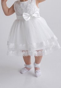 White dress with floral embroidery and pearl-accented bow. Layered tulle skirt, lace trim at hem. Matching lace socks.