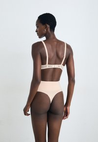 Conjunto de lingerie nude com um bralette com detalhes em renda e cuecas de cintura alta; tecido suave com uma textura lisa e design minimalista.