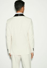 Tuxedo blanc avec col châle en satin noir et accents de boutons noirs. Texture lisse, design structuré, silhouette ajustée.