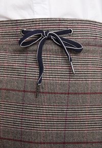 Hame plaid dengan pola campuran dalam warna abu-abu, navy, dan burgundi. Memiliki tali serut navy dengan aksen putih dan bukaan perangkat keras perak.