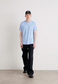 Light blue cotton t-shirt, classic fit, paired with black trousers and black shoes, model wearing a black cap. Minimalist design, plain colors.